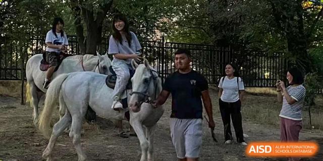 A Nord Anglia Chinese International School Shanghai student riding a white horse, with an adult walking alongside, in an outdoor setting.