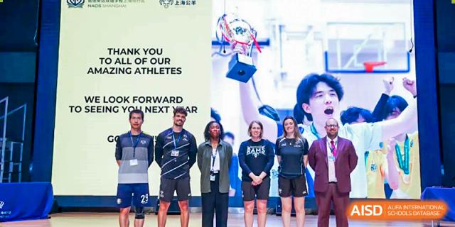 A group of Nord Anglia Chinese International School Shanghai student athletes and coaches posing with a trophy and a banner that thanks the school's athletes.