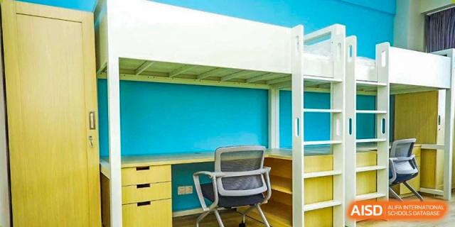 A bright, modern dormitory room at Nord Anglia Chinese International School Shanghai featuring a desk, chair, and a white loft bed structure against a blue wall.