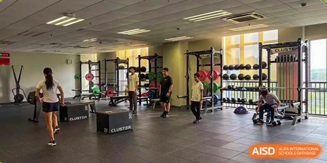 Nord Anglia Chinese International School Shanghai students and a coach working out in a well-equipped, indoor fitness center or weight room.