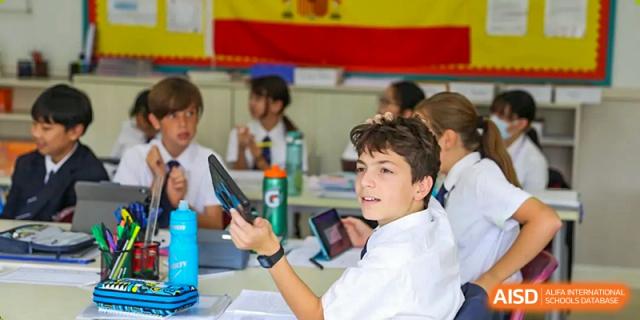 A male student smiling and raising a tablet in a group setting during a classroom discussion at Nord Anglia International School Shanghai, Pudong.