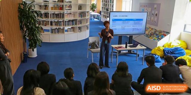 A teacher presenting to a group of seated students in a modern, circular library space with many bookshelves at Nord Anglia International School Shanghai, Pudong.