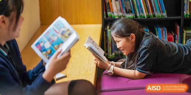 A female student smiling while reading a book in the library or classroom at Nord Anglia International School Shanghai, Pudong.