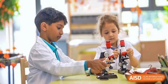 Two students in lab coats using a microscope together during a science class at Nord Anglia International School Shanghai, Pudong.