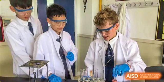 Two male students in lab coats and safety goggles conducting an experiment with beakers in a science laboratory at Nord Anglia International School Shanghai, Pudong.
