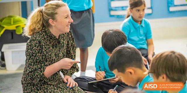 A female teacher sitting on the floor, engaging with a small group of young students at Nord Anglia International School Shanghai, Pudong.