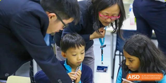 An adult closely observing a young male student who is looking intently at something during a school activity at Nord Anglia International School Shanghai, Pudong.