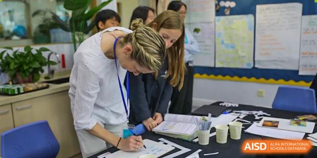 A female adult writing on a clipboard while another adult stands nearby, likely during a school fair or event at Nord Anglia International School Shanghai, Pudong.