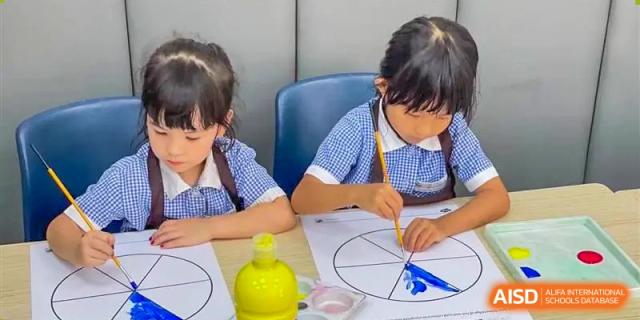 Two young female students in school uniform painting a circular diagram during an art or classroom activity at Nord Anglia International School Shanghai, Pudong.