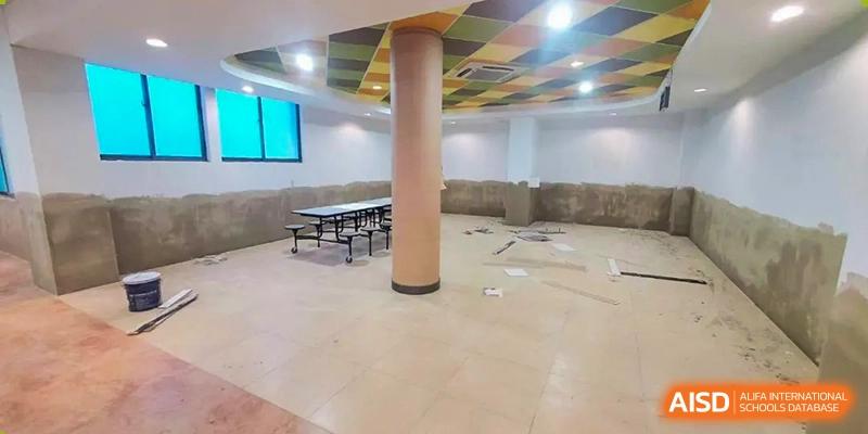 An empty, brightly lit multi-purpose room or hall with a column and tables stacked in the back at Nord Anglia International School Shanghai, Pudong.