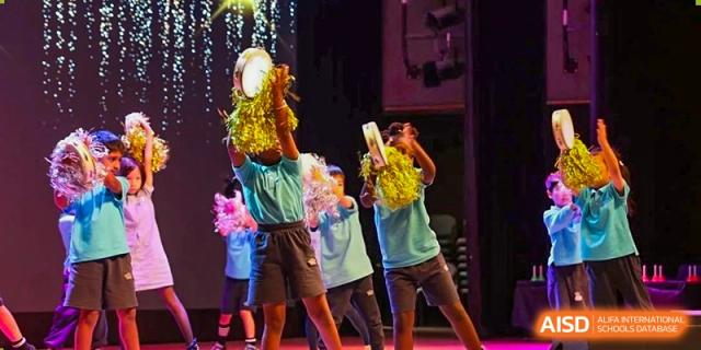 Students on stage wearing costumes and performing with tambourines and other instruments at Nord Anglia International School Shanghai, Pudong.