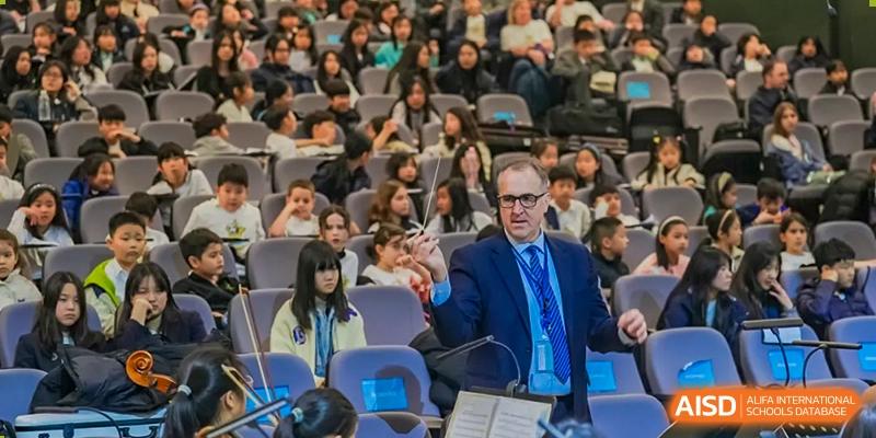 A male teacher in a suit standing in front of a large class of seated students during a lecture or presentation at Nord Anglia International School Shanghai, Pudong.