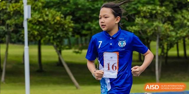 A student in a blue sports jersey with the number 16 running outdoors in a sports event at Nord Anglia International School Shanghai, Pudong.