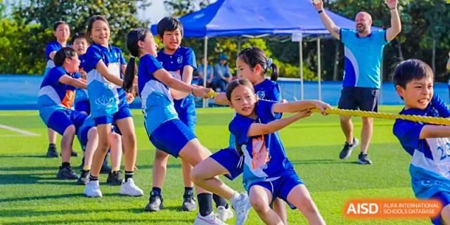 Students participating in an outdoor tug-of-war game or similar physical education activity on a sunny field at Nord Anglia International School Shanghai, Pudong.