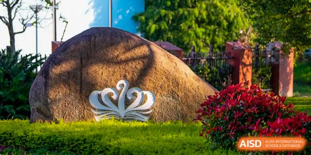 A large, decorative, crown-shaped sculpture or logo placed outdoors in a garden area at Nord Anglia International School Shanghai, Pudong.