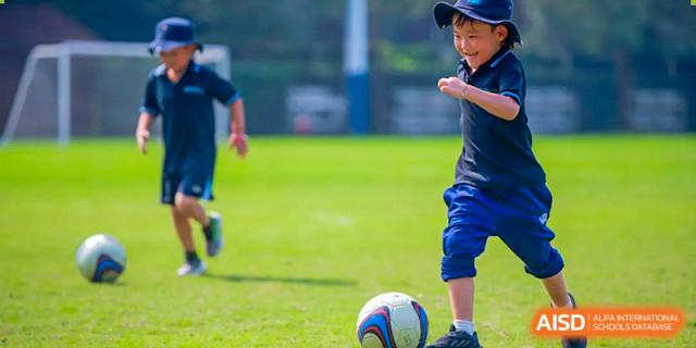 A close-up of a student in blue shorts kicking a soccer ball on a green sports field at Nord Anglia International School Shanghai, Pudong.