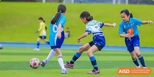 Two students competing for a soccer ball during a match on an outdoor field at Nord Anglia International School Shanghai, Pudong.