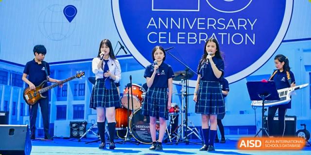 Three female students in school uniform performing on stage with microphones during an "Anniversary Celebration" event at Nord Anglia International School Shanghai, Pudong.