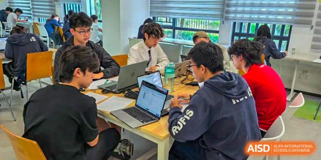 A small group of RDF International School students working collaboratively on laptops in a bright study area.