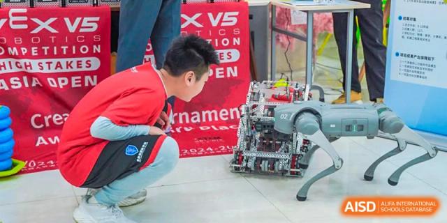 An RDF International School student kneeling and working with a robot during a VEX Robotics competition or event.