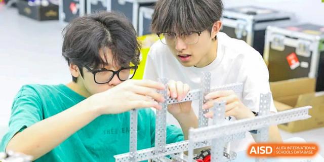 Two focused RDF International School students collaborating on building a complex metal mechanism or structure.