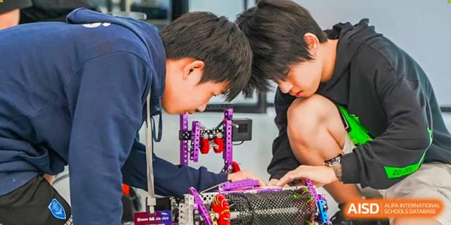 Two RDF International School students closely examining and building a component of a robot.