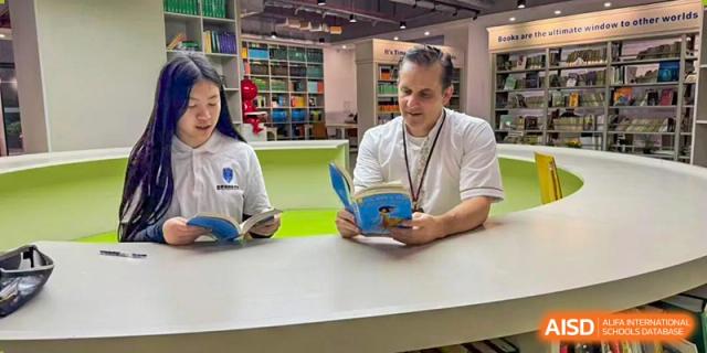 An RDF International School student and a male teacher sitting together, both reading books in the library.