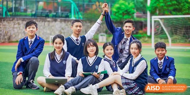A group of six smiling RDF International School students in uniform sitting together with a laptop and giving a thumbs-up.