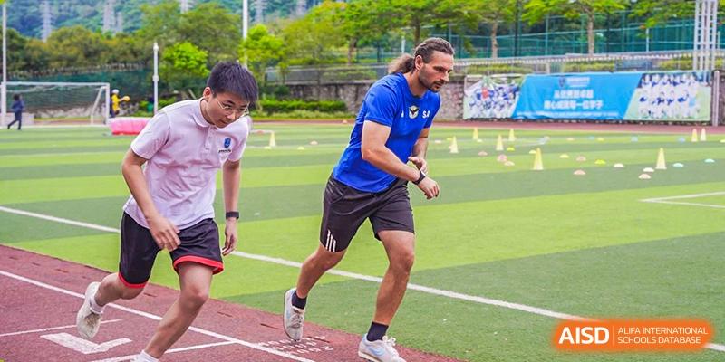 An adult coach running alongside students during a track and field exercise at RDF International School.