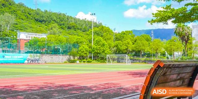 An outdoor track and field stadium with a red track and lush green surroundings at RDF International School.