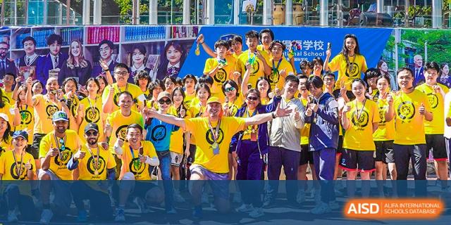 A large, energetic crowd of RDF International School students and adults celebrating at an outdoor event, with a person in a bright yellow shirt in the center.