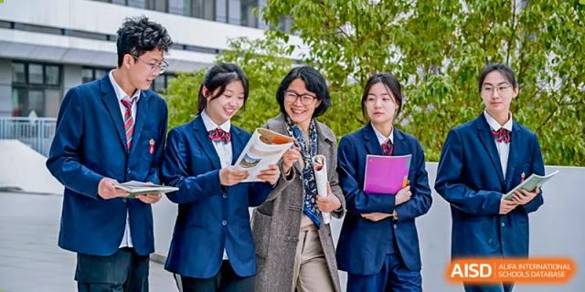 An RGS Guildford Nanjing teacher smiles while speaking with a group of female students in school blazers.