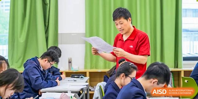 An RGS Guildford Nanjing teacher in a red shirt reviews a document with a student in a classroom setting.