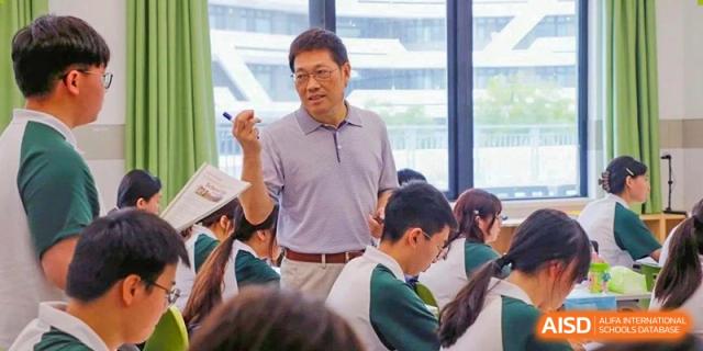 A male teacher at RGS Guildford Nanjing addresses and interacts with students seated in a classroom.