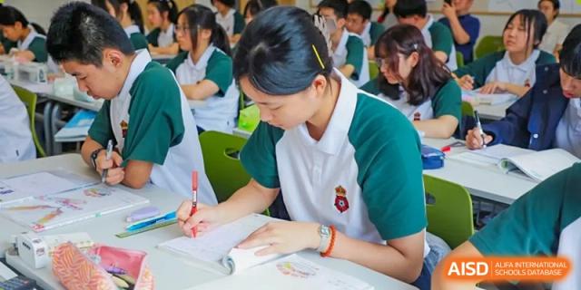 A female RGS Guildford Nanjing student in uniform focuses on writing in a notebook during class.
