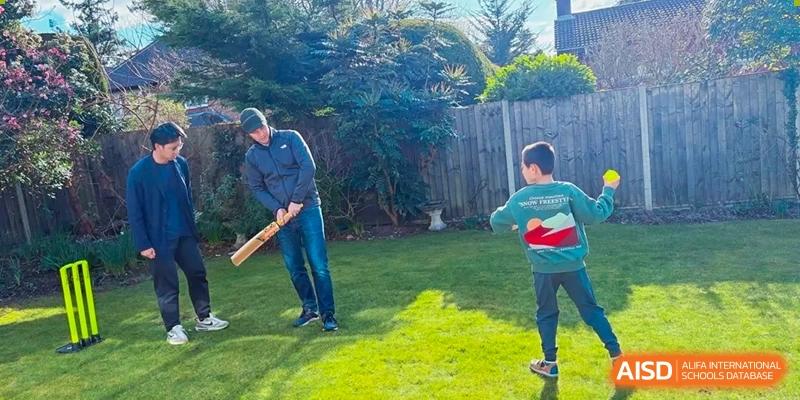 Two people playing cricket with a bat and ball in a grassy backyard, likely a recreational activity related to RGS Guildford Nanjing.