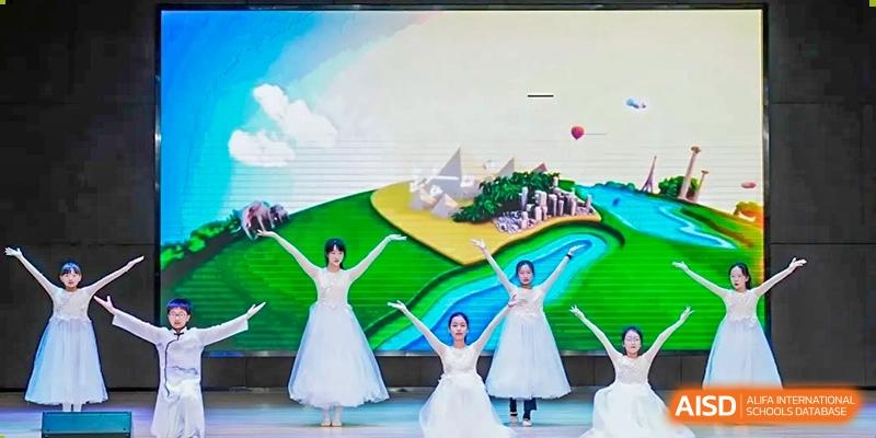 Three students in white dresses performing a dance on a colorful stage at an event for RGS Guildford Nanjing.