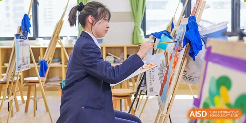A female student in uniform painting on an easel during an art class at RGS Guildford Nanjing.