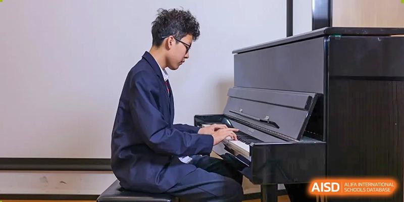 A male student in uniform playing a piano during a music lesson or practice session at RGS Guildford Nanjing.