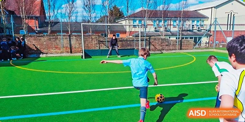 Students playing football on a green turf field during an outdoor sports class at RGS Guildford Nanjing.