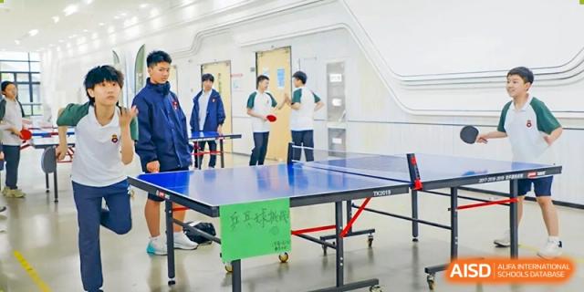 RGS Guildford Nanjing students playing table tennis in an indoor sports area with a green net sign on the table.