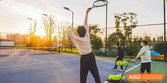 A student reaching overhead to play tennis or badminton on an outdoor court at RGS Guildford Nanjing, with the sun setting in the background.