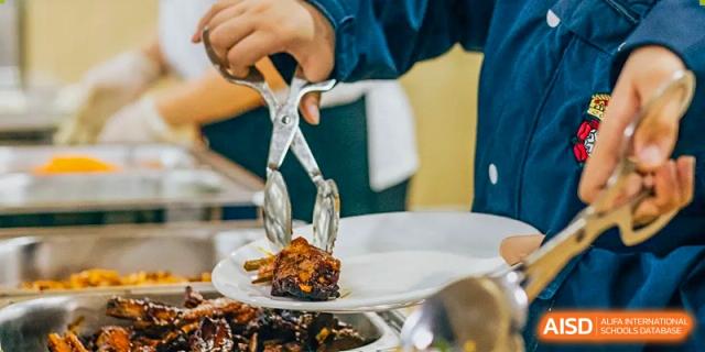 Tongs placing a piece of cooked food onto a serving plate at an RGS Guildford Nanjing event.