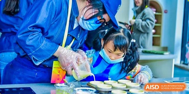 A student with a mask assisting a young child in making cookies at RGS Guildford Nanjing.