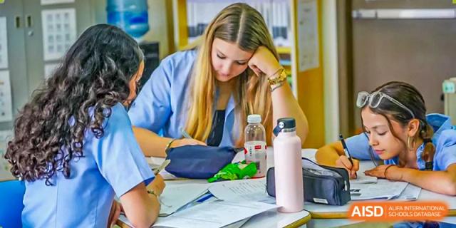 A high school or middle school female student works diligently at a desk, reviewing papers and studying at Shanghai Community International School.