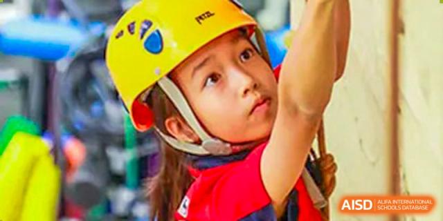 A young female student wearing a yellow safety helmet and red shirt concentrates while participating in a climbing activity at Shanghai Community International School.