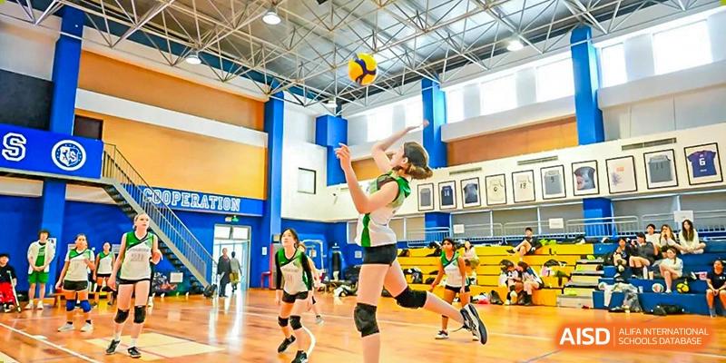 A female student in a green and white uniform jumps to spike a volleyball during a game at Shanghai Community International School.