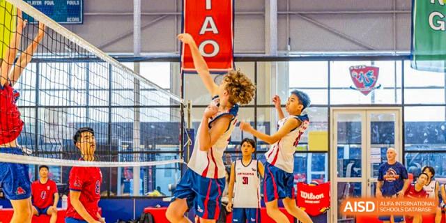 A player in a white and red uniform jumps high to hit a volleyball over the net during an intense game at Shanghai Community International School.