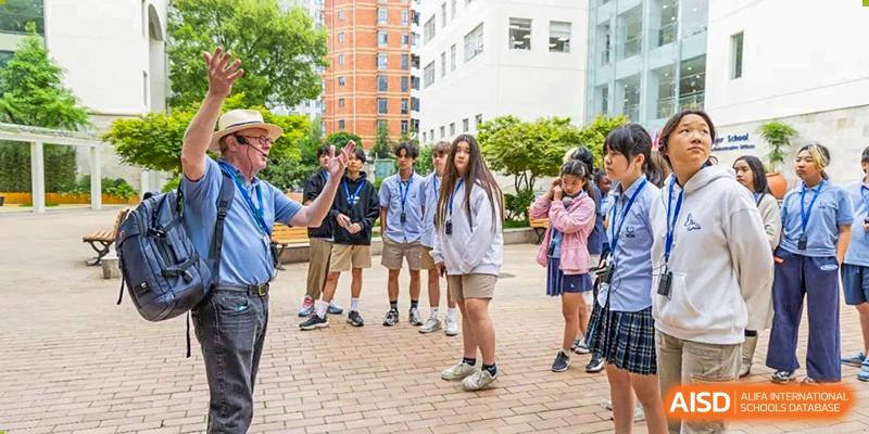 A diverse group of middle and high school students stand outside on a sunny brick patio during a break or social activity at Shanghai Community International School.