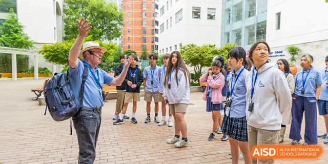 A diverse group of middle and high school students stand outside on a sunny brick patio during a break or social activity at Shanghai Community International School.